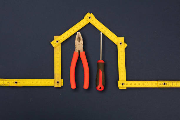 Home repair. Hand tools under house shape yellow wooden measure, black background. Folding ruler and hardware, workshop, construction, renovation concept.