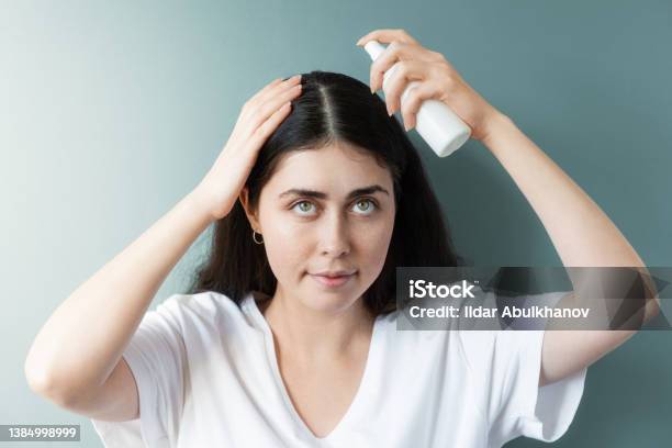 Portrait Of A Caucasian Woman With Dark Hair Applying Spraying Cosmetic  Product To The Hair Parting