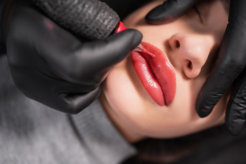 Close-up of swollen female lips during the application of permanent makeup. Tattoo on the face and micropigmentation of the lips. Professional facial microblading.