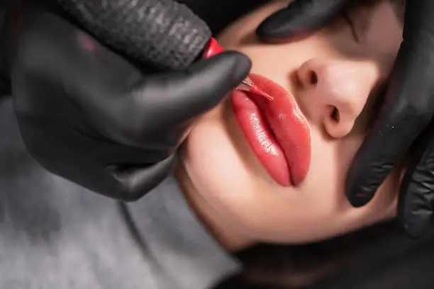 Close-up of swollen female lips during the application of permanent makeup. Tattoo on the face and micropigmentation of the lips. Professional facial microblading. Female cosmetology apparatus.