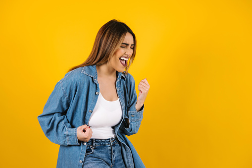 young latin woman gesturing YES, celebrating success or achievement, feeling excited on yellow background