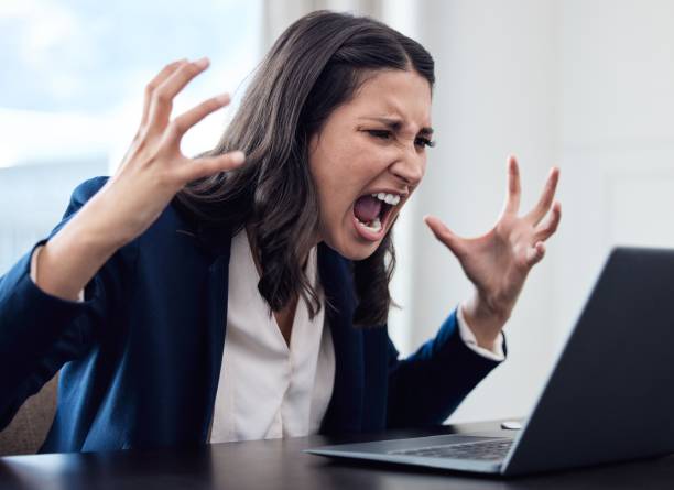 shot of a young businesswoman yelling while using a laptop in an office at work - furious imagens e fotografias de stock