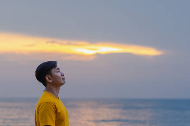 Asian man smiling and looking up with sea and sky background. Good mental health concept.