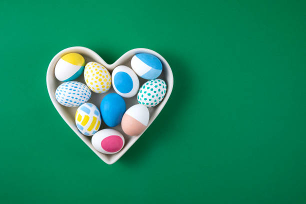 istock Colorful Easter Eggs in Heart Shaped Bowl on Green Background 1385049416