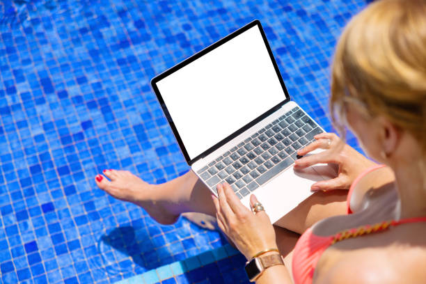 istock Woman working with laptop at poolside, screen mockup 1385053557