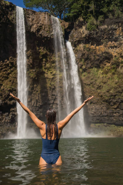 istock Young woman wades through pool under waterfall 1385057348