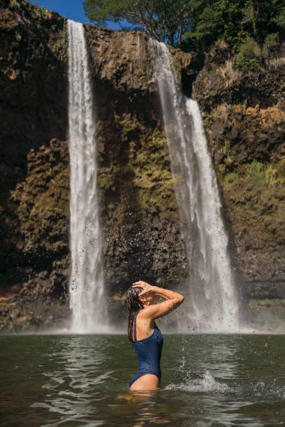 istock Young woman goes for a swim under waterfall 1385057349
