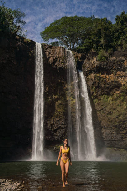 istock Young woman wades through pool under waterfall 1385058781