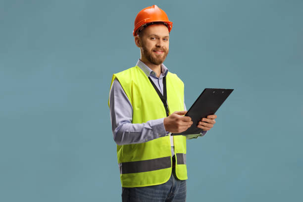 istock Site engineer wearing a reflective vest and helmet holding a clipboard and looking at camera 1385061888