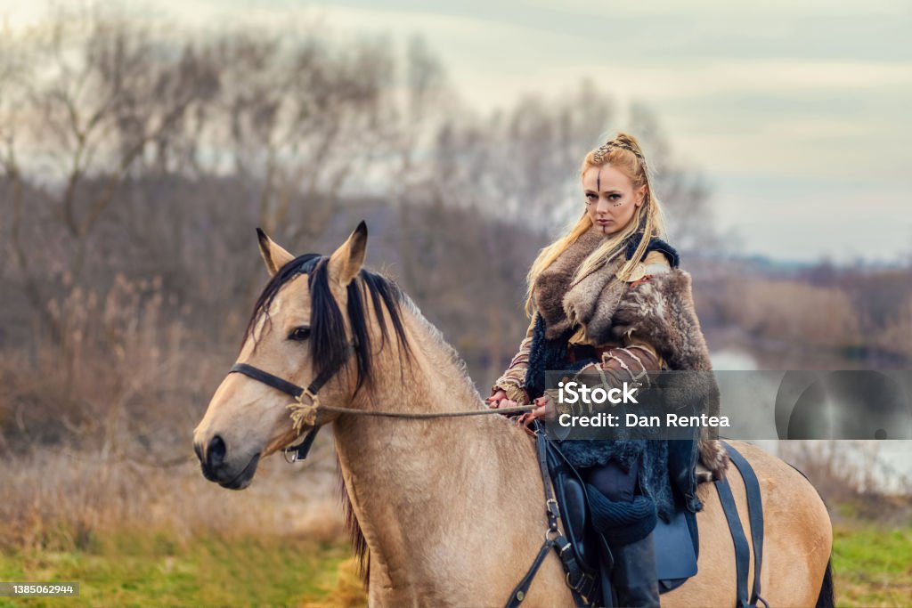 Beautiful Viking warrior royal female riding horse Beautiful Viking warrior royal female with braids and painted face riding horse in forest Medieval Stock Photo