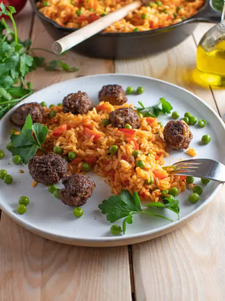 Delicious mediterranean or balkan food with djuvec rice and spicy fried meatballs. Served on a white plate on wooden table background. Ready to eat, Vertical image