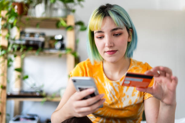 une jeune femme aux cheveux colorés fait ses courses en ligne avec une carte de crédit - women currency white savings photos et images de collection
