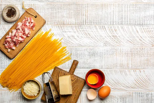 Ingredients fortraditional  italian pasta carbonara, spaghetti, pancetta, egg yolk, black pepper and parmesan cheese on white wooden surface. Copy space.