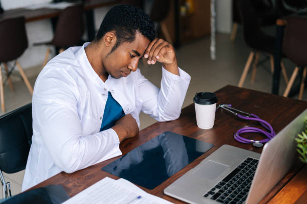 istock Tired African black male doctor working on laptop, thinking about problem and drinking coffee. 1385068853