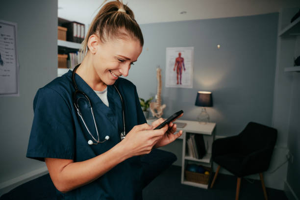 istock Caucasian female nurse typing on cellular device standing in doctors office 1385071915