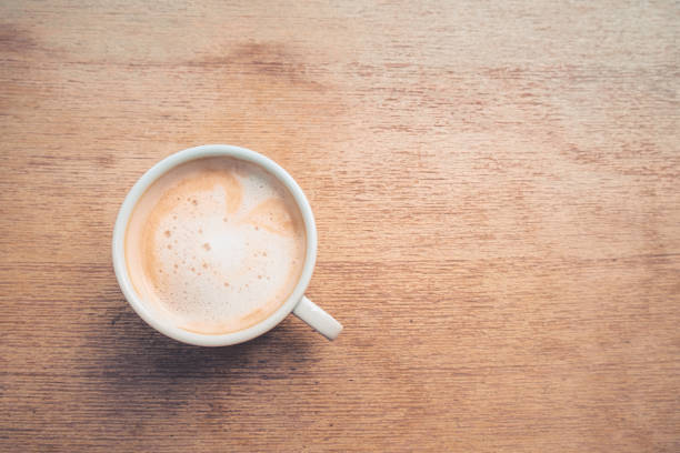 Hot cappuccino the best start to any morning in the cafe Above view of hot cappuccino art on wooden table at the coffee shop. White cup of coffee the best start to any morning at the cafe. Top-down coffee table top stock pictures, royalty-free photos & images