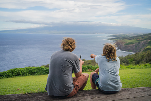 They sit on outdoor patio and fly the drone over the Pacific Ocean in the distance