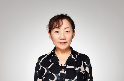 An elderly East Asian woman in a black shirt looks at the camera. The studio shot against a white background.There was an expression of concentration on her face