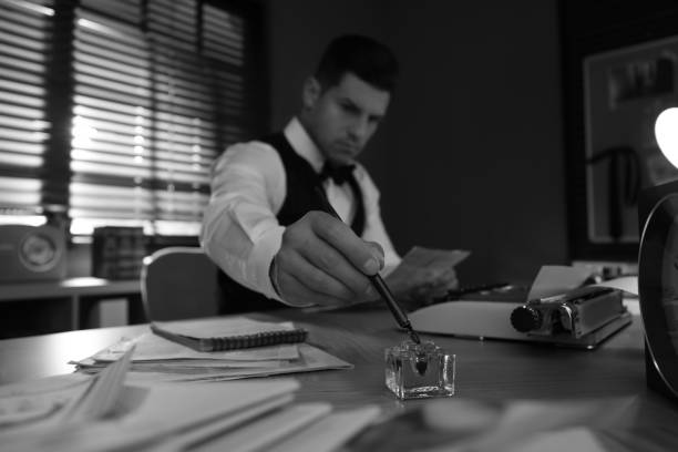 istock Old fashioned detective working at table in office, focus on hand with ink pen. Black and white effect 1385080187