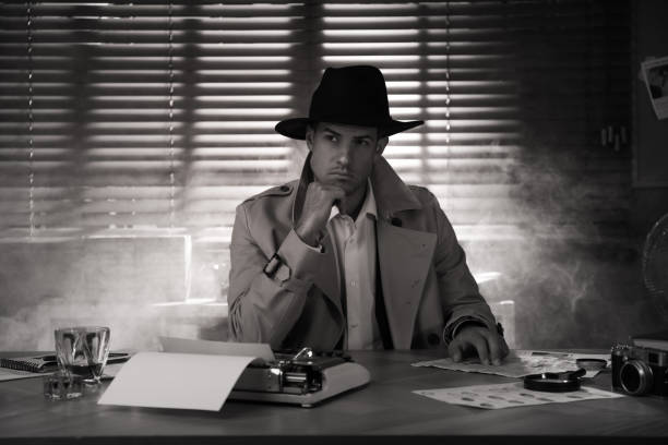 istock Old fashioned detective at table in office. Black and white effect 1385080217