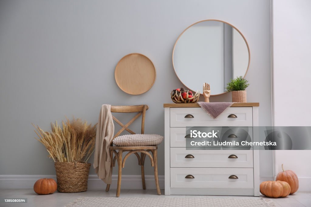 Round mirror and chest of drawers near grey wall in hallway. Interior design Dresser Stock Photo