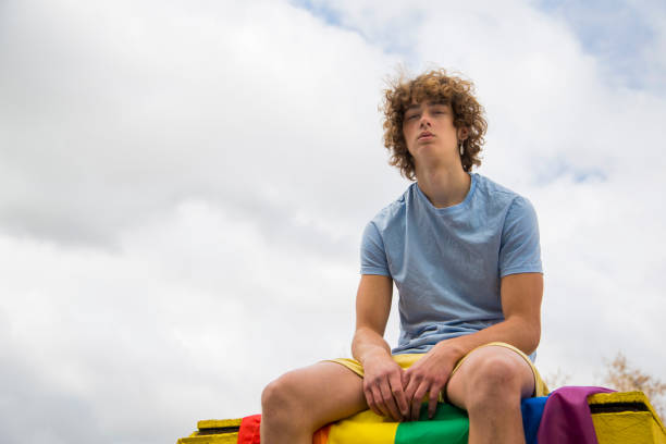 istock gay guy posing sitting on a gay pride flag 1385083035