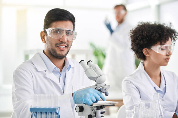 istock smiling scientist sitting in front of a laboratory microscope 1385084968