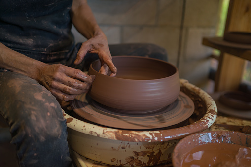 He shapes the wet clay into a pot formation, as it spins on table