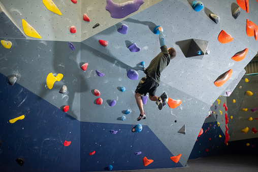 Back view of man training. Sportsman in dark clothes at bouldering wall. Sport, hobby, wellbeing concept