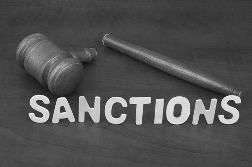 Broken wooden judge gavel and word sanctions close up.