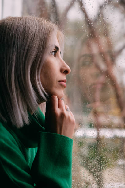 istock Depressed Woman Watching the Rain Through the Window 1385087342