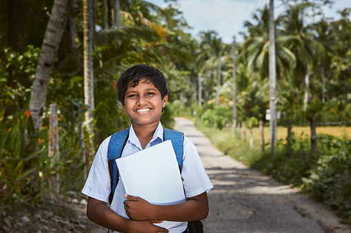 Schoolboy in uniform is walking to school. Portrait boy on rural road in Sri Lanka.\