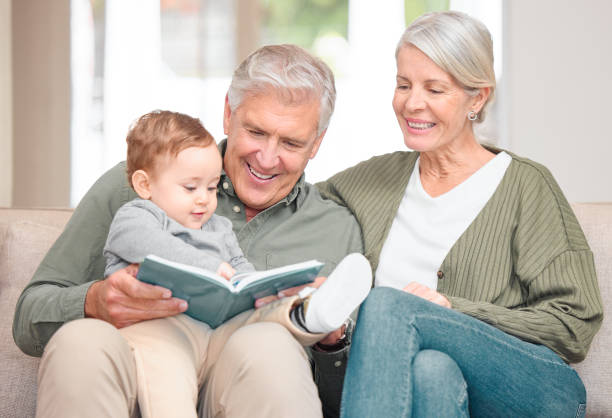 przycięte ujęcie czułej pary seniorów czytającej wnukowi siedząc na kanapie w domu - grandmother reading child grandson zdjęcia i obrazy z banku zdjęć