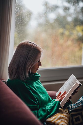 Woman Reading a Book in Front of the Window in the Rainy Day