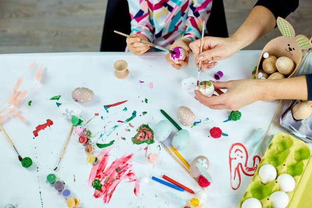 istock Top view unrecognizable mother and her daughter in easter holiday coloring easter eggs 1385090357