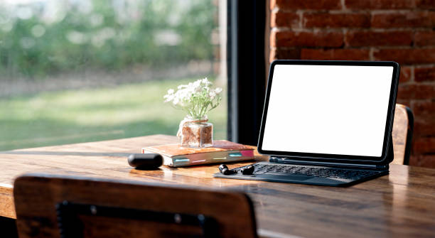 istock Open blank screen tablet computer in comfortable workspace with gadget and flower pot. 1385090648