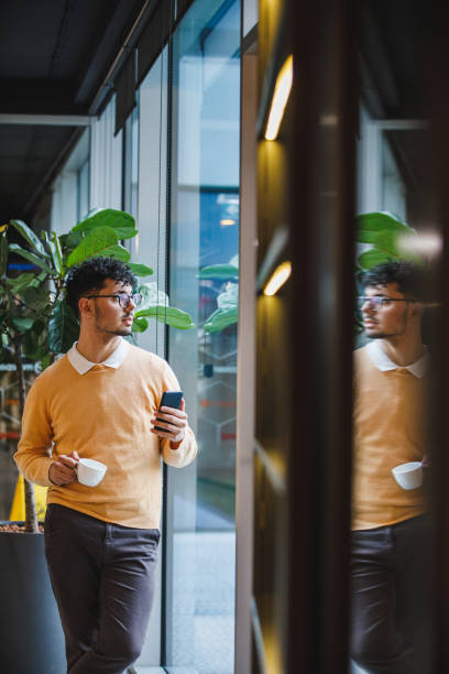 istock Businessman on a coffee break using smart phone, looking through the window 1385092145