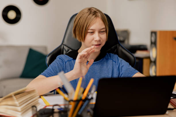 istock A boy attending an elementary school has lessons with his teacher remotely via the Internet, the child waves to laptop camera to greet classmates, a desk prepared in the study room 1385092374