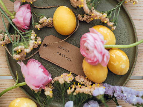 Yellow natural colored easter egg and flowers with text happy easter
Photo taken indoors in natural sunlight of eggs colored with turmeric