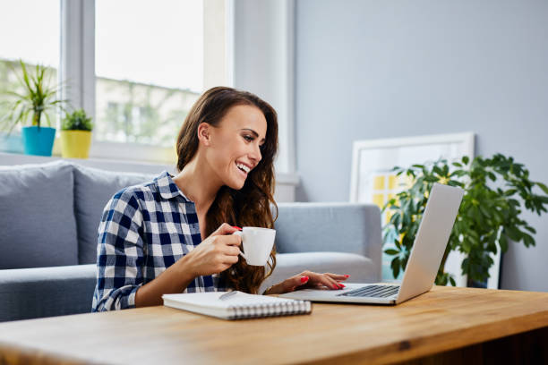 istock Happy young woman drinking coffee using laptop at home 1385095263