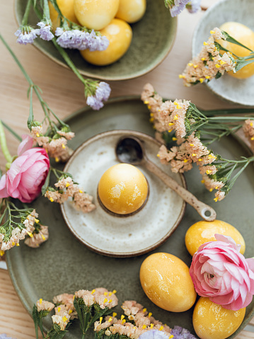 Yellow natural colored easter egg and flowers arrangement\nPhoto taken indoors in natural sunlight of eggs colored with turmeric