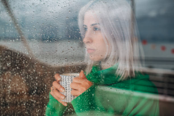 istock Depressed Woman Watching the Rain Through the Window 1385095753