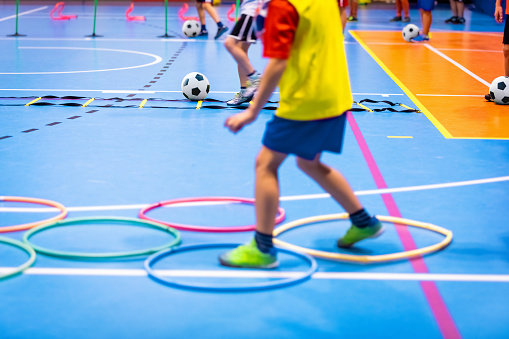 Clase de fútbol sala para niños en el pabellón de deportes escolar. Niños pateando pelotas de fútbol en el piso de fútbol sala de madera. Práctica deportiva de fútbol para niños en edad preescolar photo