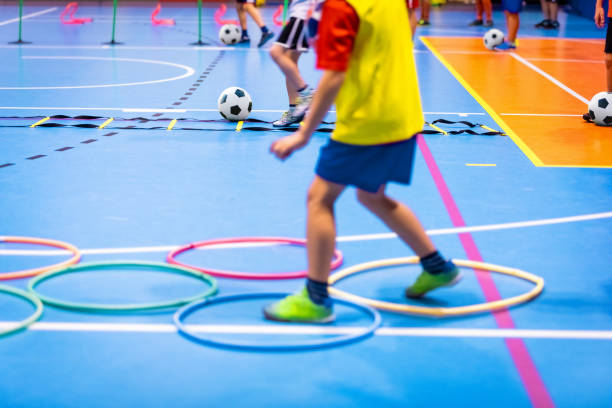 corso di calcio indoor per bambini presso il palazzetto dello sport della scuola. bambini che calciano palloni da calcio sul pavimento di futsal in legno. pratica sportiva di calcio per ragazzi in età prescolare - gara sportiva giovanile foto e immagini stock