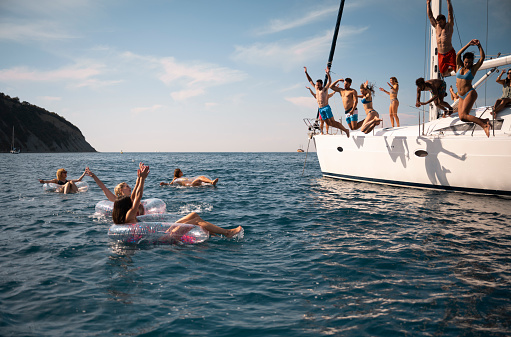 Young friends relaxing on floats and jumping in sea.