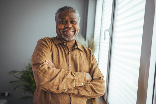 African American Senior Man at home Portrait. African American Senior Man at home Portrait. Smiling senior man looking at camera. Portrait of black confident man at home. Portrait of a senior man standing against a grey background african ethnicity stock pictures, royalty-free photos & images