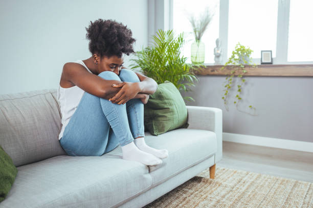 joven atractiva mujer afroamericana acostada en el sofá de la sala de estar de su casa sintiéndose triste y cansada - bad conditions fotografías e imágenes de stock