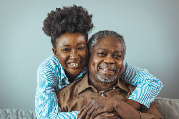 Portrait of a daughter holding her elderly father Senior man and his middle aged daughter smiling at each other embracing, close up. Portrait of a daughter holding her elderly father, sitting on a bed by a window in her father's room. heavy photos stock pictures, royalty-free photos & images