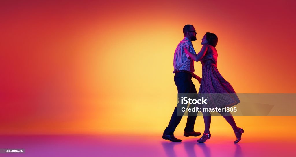 Portrait of excited man and woman, couple of dancers in vintage retro style outfits dancing lindy hop dance isolated on gradient yellow and purple background. Flyer Flyer. Portrait of excited man and woman, couple of dancers in vintage retro style outfits dancing lindy hop dance isolated on gradient yellow and purple background. Concept of art, action, motion. Dancing Stock Photo
