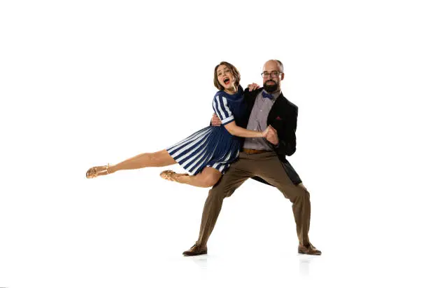 Photo of Couple of dancers, young man and woman in vintage retro style outfits dancing swing dance isolated on white background. Timeless traditions, 60s, 70s fashion style.